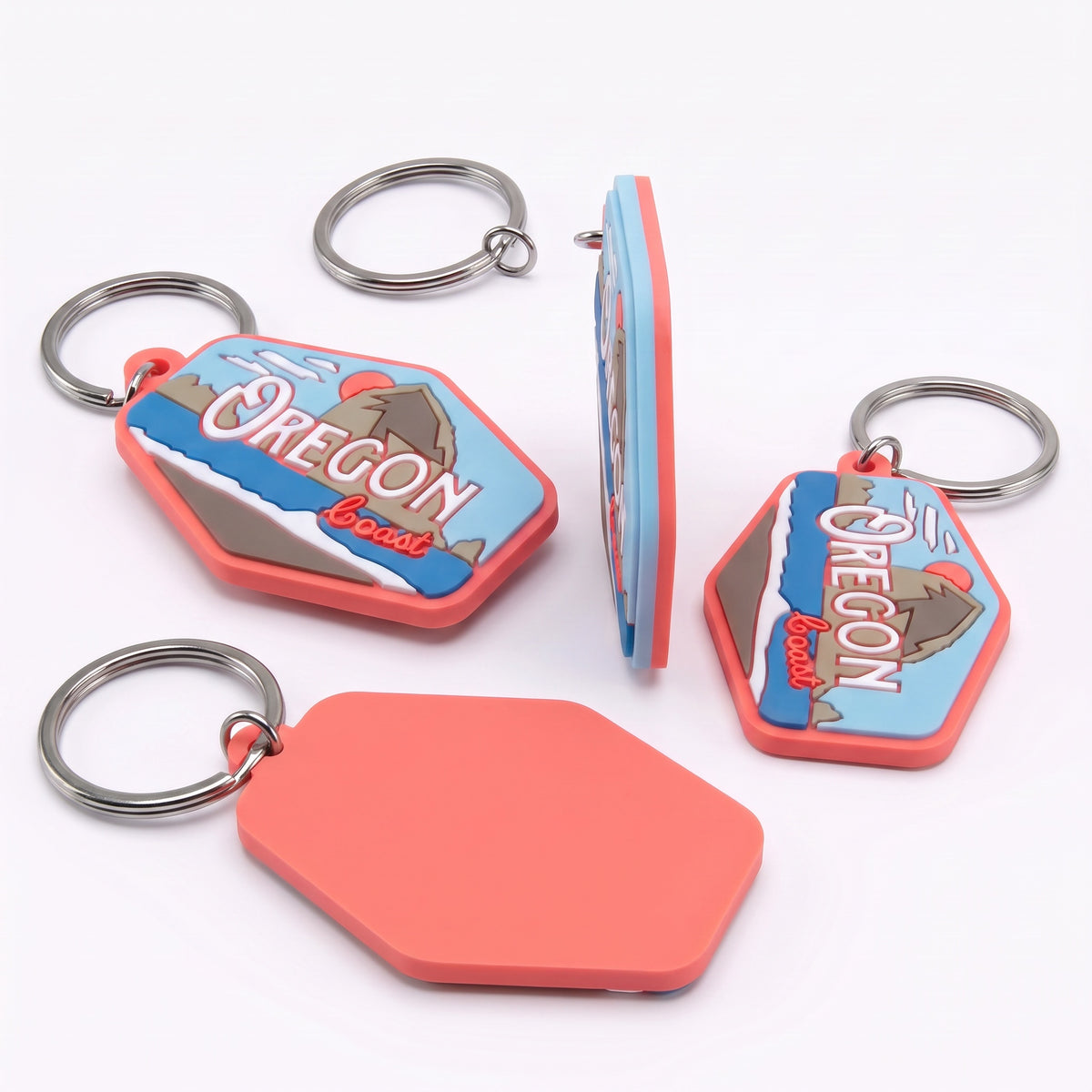 Four views of a silicone keychain featuring an Oregon border design, including a front view with a metal key ring, a side view, a back view with a blank coral-colored silicone panel, and another front view. The keychain has a blue and white Oregon border graphic with a mountain illustration, surrounded by a coral-red border, on a white background.